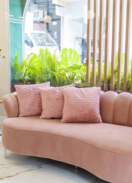 Lounge de espera com sofá rosé, almofadas e plantas