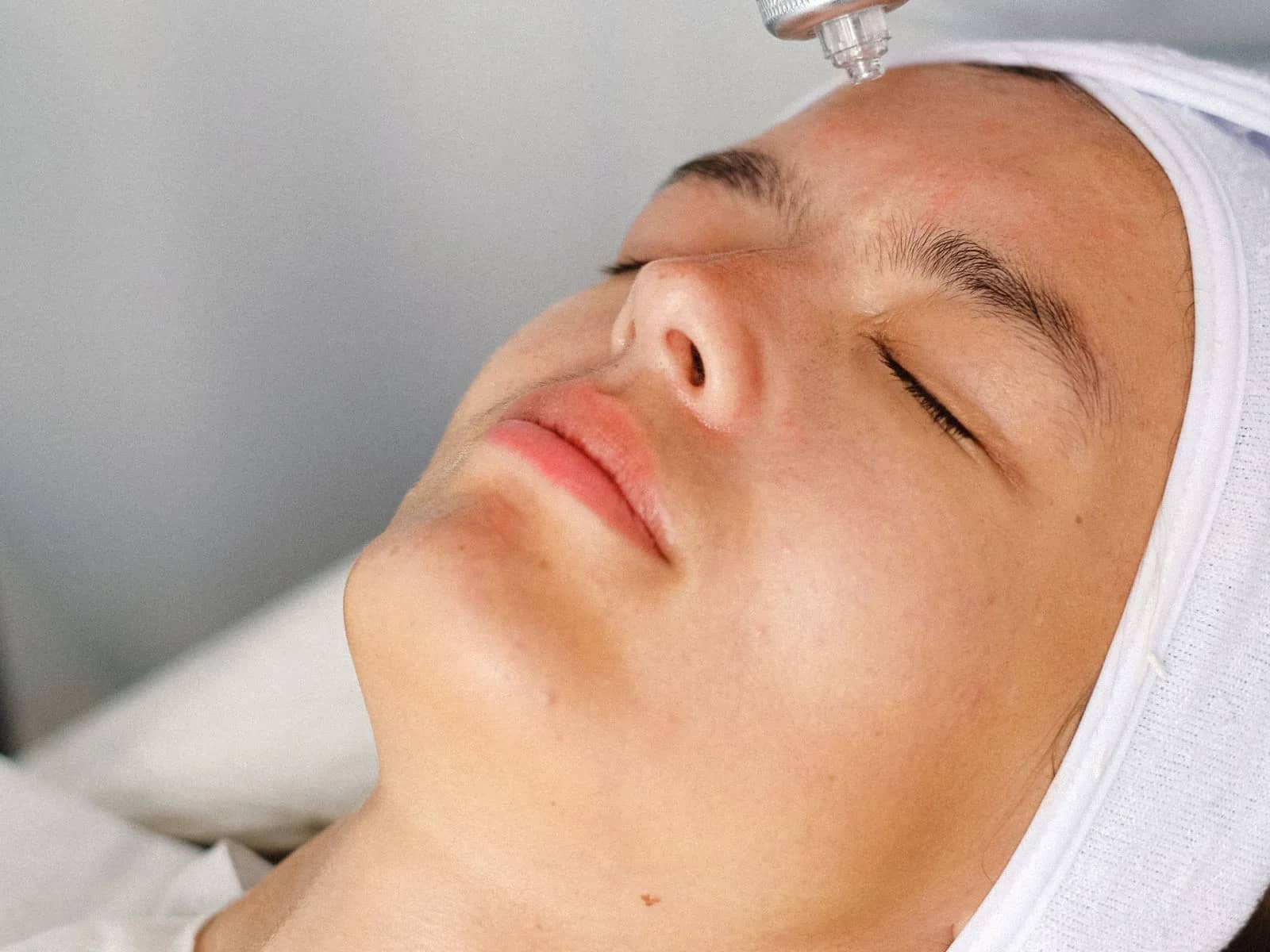Mulher deitada de olhos fechados recebendo cuidado facial em cabine de estética